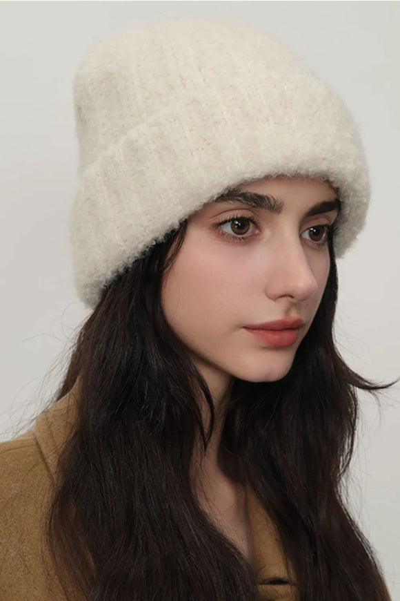 Woman wearing a cream-colored knit hat against a plain background