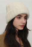 Woman wearing a cream-colored knit hat against a plain background