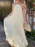 Woman in a white pleated dress holding a straw bag outdoors.