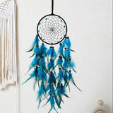 Blue feather dreamcatcher hanging against a white wall with macrame wall art.