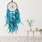 Blue feather dreamcatcher hanging on a white wall with a wooden table and decorative items below.