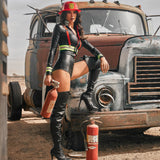 Woman in a black leather firemans outfit with red helmet standing next to an old, rusted truck in a desert setting.