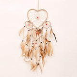 Heart-shaped dreamcatcher with feathers on a light pink background