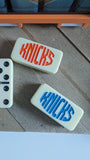 Two dominos with 'KNICKS' printed on them, one in red and one in blue.